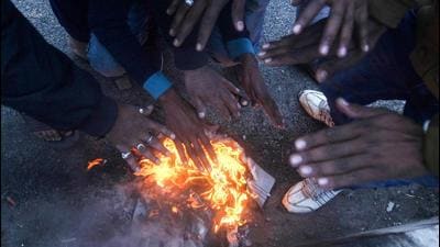 People warm themselves next to a fire during a cold winter morning. (PTI)