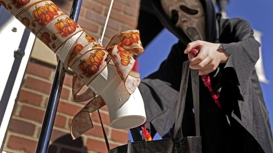 A boy gets candy via a plastic pipe to help prevent the spread of the novel coronavirus as he trick-or-treats for Halloween Saturday, October 31, 2020, in downtown Overland Park, Kan. (AP Photo/Charlie Riedel))