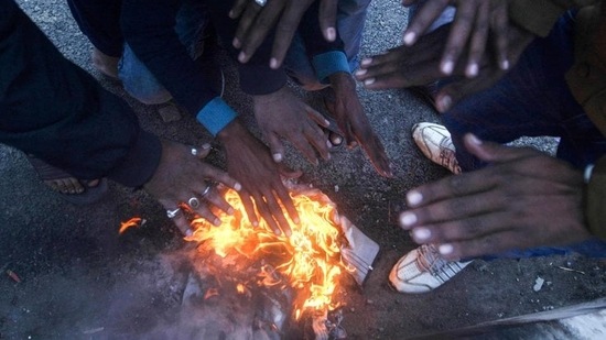 People warm themselves next to a fire during a cold winter morning.&nbsp;