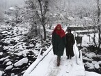 Locals cross a snow-covered bridge in Srinagar on Tuesday.(Waseem Andrabi/HT Photo)