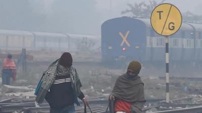 People cross railway tracks amid low visibility due to fog on a cold winter morning in New Delhi on Tuesday. (PTI)