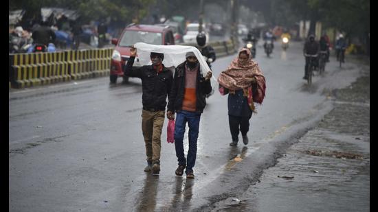 Pedestrians use a piece of plastic sheet to cover themselves from rain, on a stretch at Sector 10A in Gurugram on Saturday. (Parveen Kumar/HT)