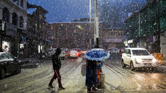 People walk with umbrellas during snowfall, in Srinagar on Friday.(PTI Photo)