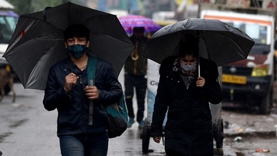People in Delhi walk under umbrellas amid rainfall on Sunday. (ANI Photo)