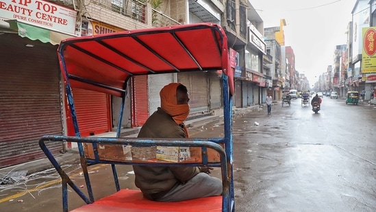 A rickshaw puller sits on his rickshaw at Laxmi Nagar Market during weekend curfew imposed to contain the spreading of Covid-19 and Omicron cases, in New Delhi. (ANI Photo)