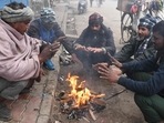 Vendors warm themselves around a bonfire during a cold foggy morning.