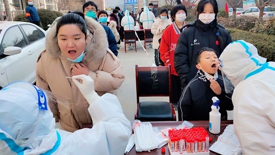 Medical workers wearing protective suits swab a woman and a child for a coronavirus test in Huaxian County in central China's Henan Province.(AP)