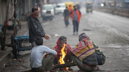 People huddle around a bonfire during light rainfall at Sadar Bazar in New Delhi.(HT Photo)
