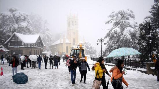 Tourists and locals take a stroll amid snowfall on The Ridge in Shimla on Sunday. More than 730 roads, including four national highways, have been blocked for traffic in Himachal due to the inclement weather. (Deepak Sansta / HT)