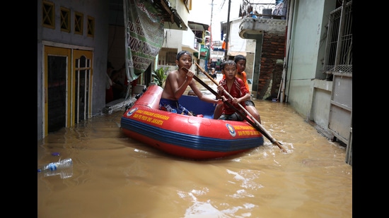 Youths use an inflatable raft to move through a flooded neighborhood in Jakarta, Indonesia, 2020 (AP)