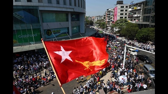 The flag of the National League for Democracy party flies over protesters taking part in a demonstration against the February 1 military coup in Yangon on February 10, 2021 (AFP)