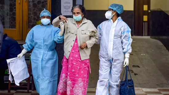 Health workers help a patient after her discharge from a state government-run Covid-19 hospital.(PTI)