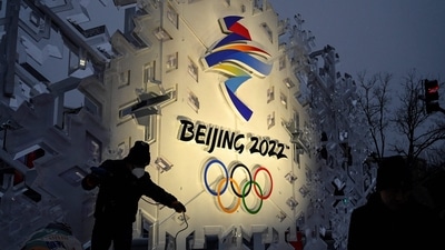 This file photo taken on January 21, 2022 shows workers setting up an installation displaying the logo of the Beijing 2022 Olympic Games on a street in Beijing. - The "curse" of Olympic overspending looks set to strike again at the Beijing Games, with stringent Covid measures and loss of ticket sale revenues pushing up costs for China. &nbsp; (Photo by JADE GAO / AFP)