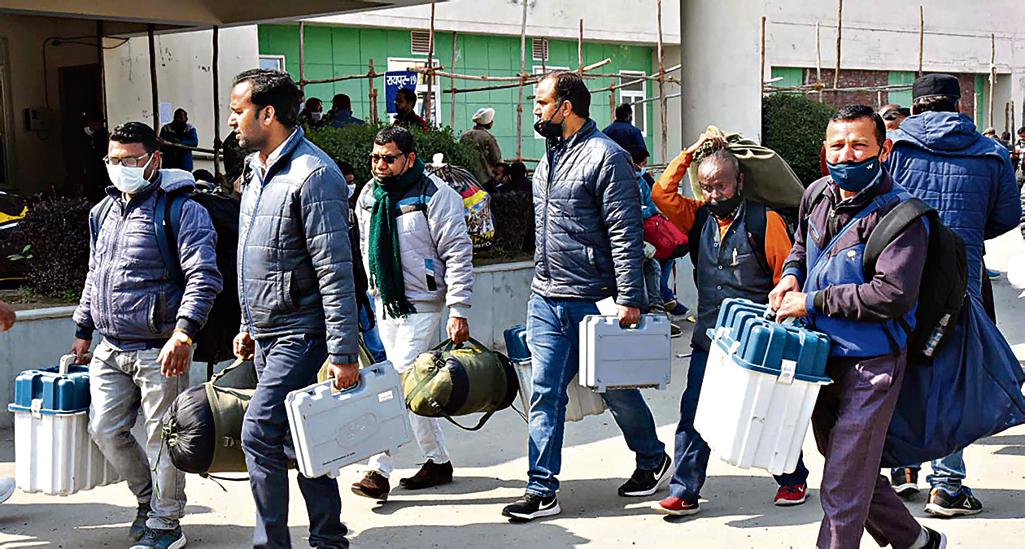 Polling officials carrying the Electronic Voting Machine (EVMs) and other necessary inputs required for the Uttarakhand Assembly Election, at a distribution centre, in Dehradun on Sunday. February 13, 2022. (ANI Photo)