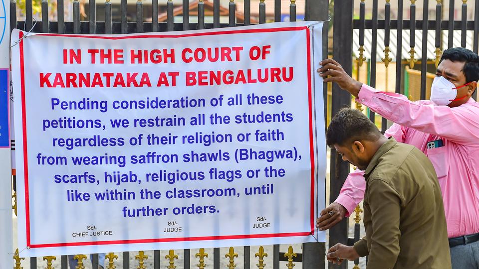 School staff places a banner with high court's interim order over hijab issue, on the entrance of Desheeya Vidhyashala Samithi PU College, in Shivamogga, on Friday. (PTI) School staff places a banner with high court's interim order over hijab issue, on the entrance of Desheeya Vidhyashala Samithi PU College, in Shivamogga, on Friday. (PTI)