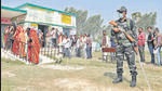 Security personnel guard a polling booth as people stand in queues to cast their votes during the third phase of UP elections, in Saifai, on Sunday. The third phase saw a voter turnout of 57.58% till 5 pm. (HT photo)