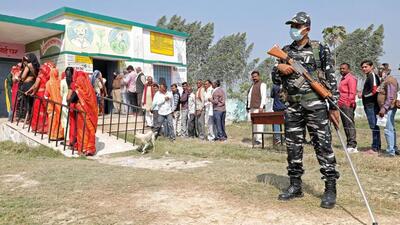 A security personnel stands guard at a polling station as voters wait in queues to cast their votes for the third phase of Uttar Pradesh assembly election, at Saifai, in Etawah on Sunday. (ANI PHOTO)