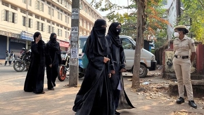 Hijab-wearing students arrive to attend classes as a policewoman stands guard outside a government girls school after the recent hijab ban, in Udupi town in Karnataka (Reuters)