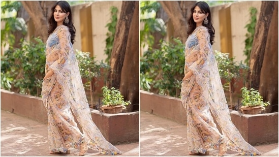 The blush pink georgette saree comes adorned with floral print in yellow, orange, blue and green shades, beadwork on the borders running across the hem and pallu, and dangling tassels. She teamed it with a pastel blue cropped bralette featuring barely-there straps, beadwork on the bust, tie up at the back, and a V neckline.(Instagram/@rhea_chakraborty)