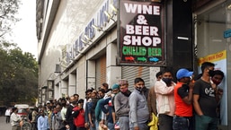 नई दिल्ली रेलवे स्टेशन पर रविवार को शराब की कीमतें कम होने के कारण लोग एक शराब की दुकान के बाहर कतार में खड़े हैं।  (एएनआई फोटो)