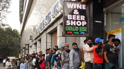 People stand in a queue outside a liquor store as prices of liquor were reduced at New Delhi Railway Station, on Sunday. (ANI Photo) People stand in a queue outside a liquor store as prices of liquor were reduced at New Delhi Railway Station, on Sunday. (ANI Photo)