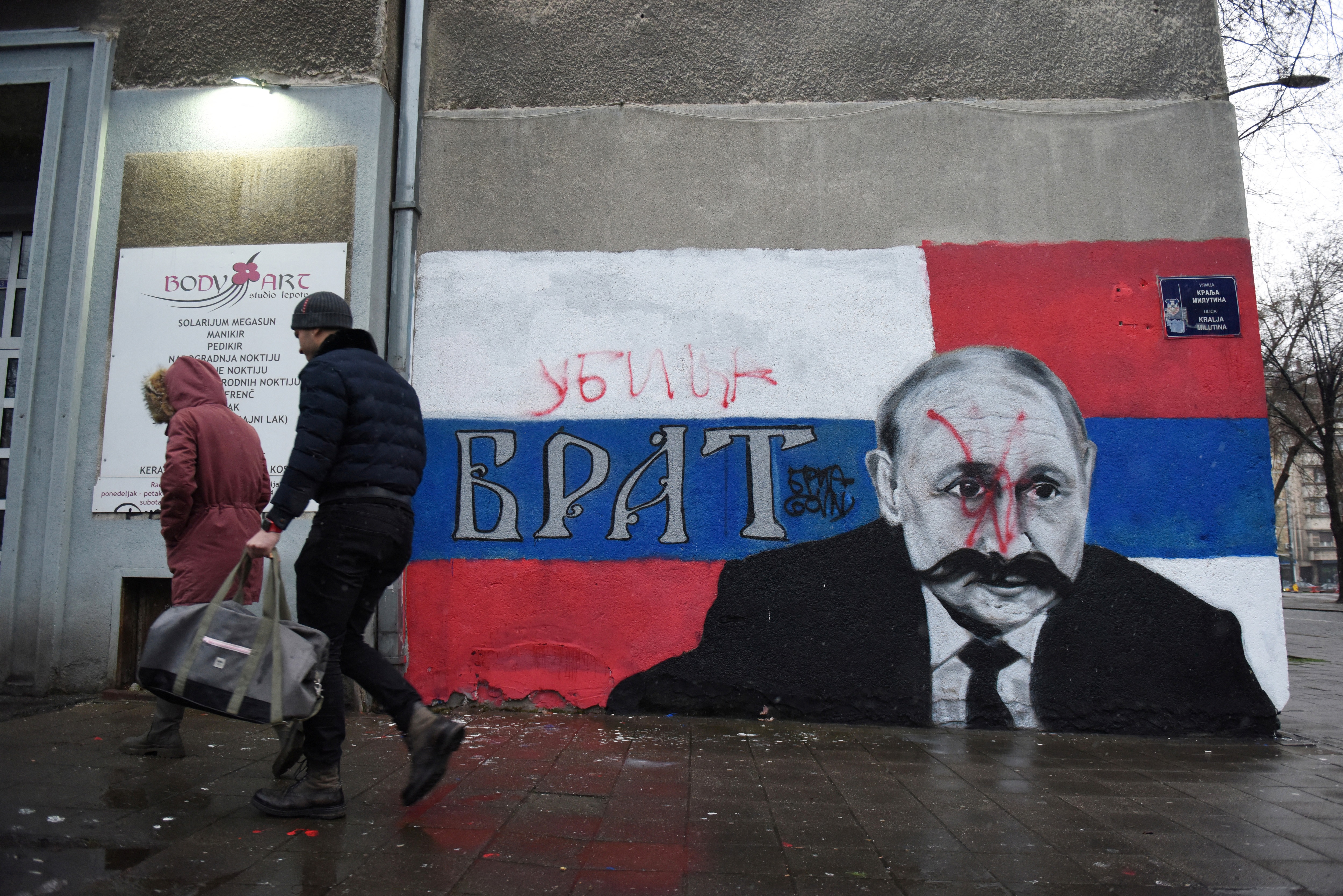 People walk next to a mural of Russian President Vladimir Putin, which has been vandalised with red spray paint and the word "Murderer" written above the original text reading: "Brother", in Belgrade, Serbia. (REUTERS)