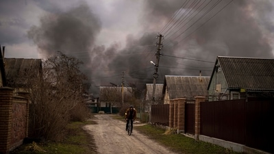 A Ukrainian man rides his bicycle near a factory and a store burning after it had been bombarded in Irpin, on the outskirts of Kyiv, Ukraine. (AP)