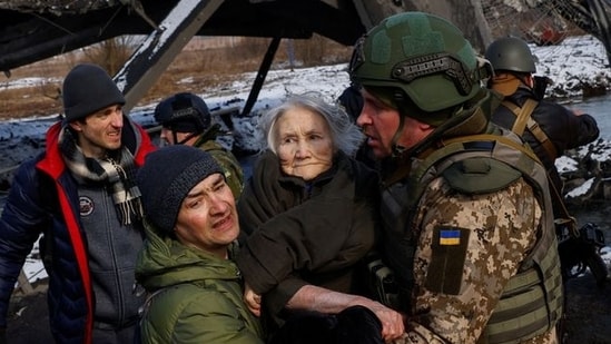 Two men carry a woman as people flee from advancing Russian troops in the town of Irpin outside Kyiv.(REUTERS)