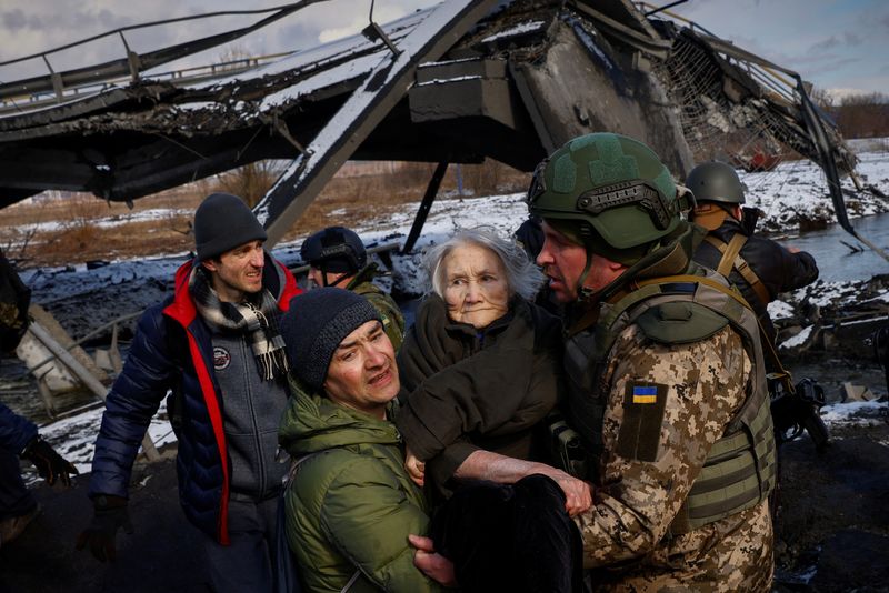Two men carry a woman as people flee from advancing Russian troops in the town of Irpin outside Kyiv. (REUTERS)