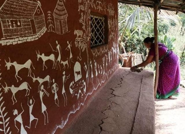 Women works outside her house that is painted with Warli art Women works outside her house that is painted with Warli art