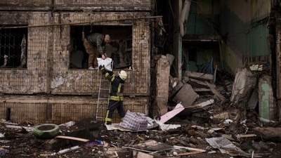 A Ukrainian firefighter helps a man remove belongings from a destroyed building after it was hit by artillery shelling in Kyiv, Ukraine, Monday. (AP Photo)