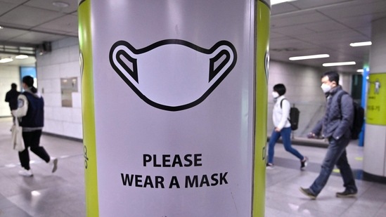 People walk past a poster showing precautions against the Covid-19 coronavirus at a subway station in Seoul on March 17, 2022, after South Korea's daily infections rose sharply to hit a new high of over 600,000. (Jung Yeon-je / AFP)(AFP)