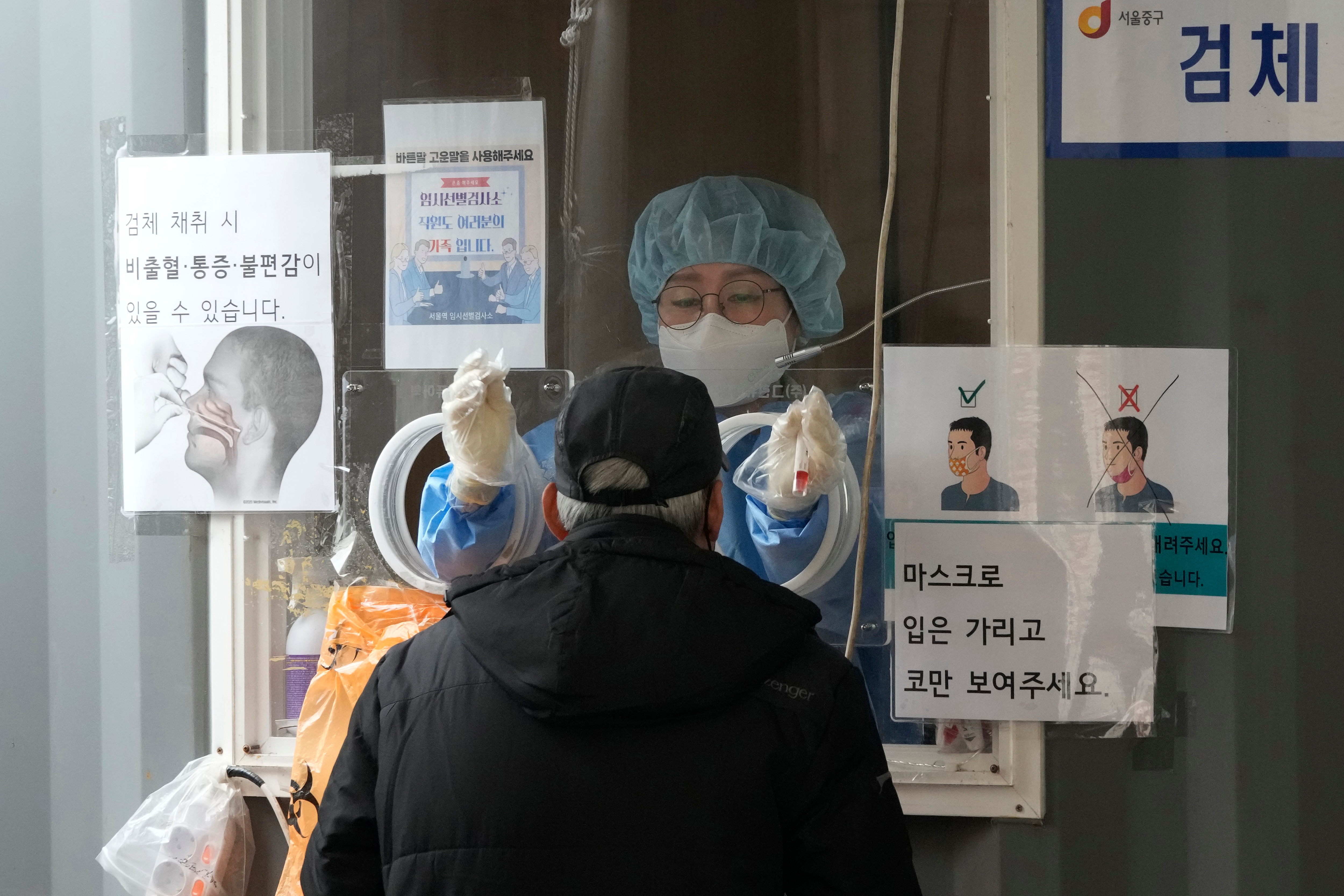 A medical worker in a booth prepares to take a nasal swab sample from a man at a makeshift testing site in Seoul, South Korea on March 17, 2022.&nbsp; (AP Photo)