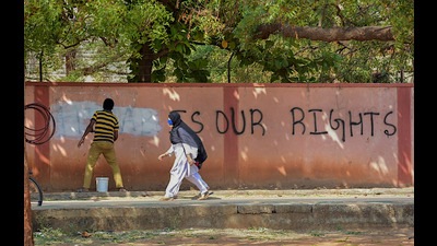 A hijab-wearing student walks past a worker painting a wall to conceal a pro-hijab slogan, Hospet, March 16, 2022 (PTI) A hijab-wearing student walks past a worker painting a wall to conceal a pro-hijab slogan, Hospet, March 16, 2022 (PTI)