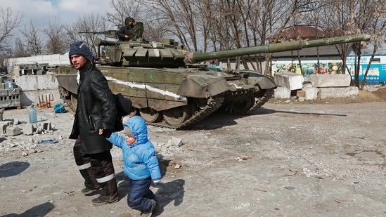 A local resident walks with a child past a tank of pro-Russian troops during Ukraine-Russia conflict in the besieged southern port city of Mariupol, Ukraine.