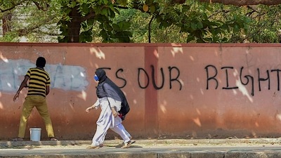 A hijab-wearing student walks past a worker painting a wall to conceal a pro-hijab slogan, Hospet, March 16, 2022 (PTI) (HT_PRINT) A hijab-wearing student walks past a worker painting a wall to conceal a pro-hijab slogan, Hospet, March 16, 2022 (PTI) (HT_PRINT)