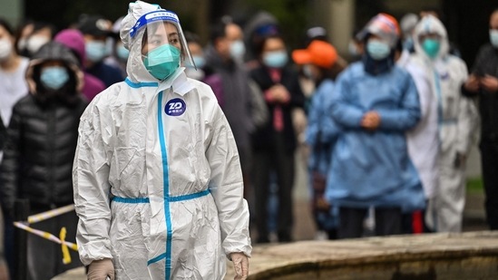 A worker wearing protective gear looks on as people wait to be tested for the Covid-19 coronavirus at a residential compound in Shanghai.(AFP)