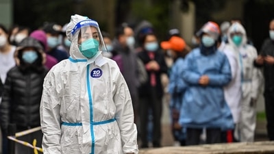 A worker wearing protective gear looks on as people wait to be tested for the Covid-19 coronavirus at a residential compound in Shanghai. (AFP)