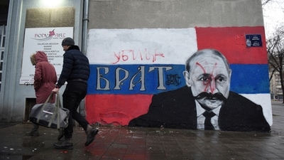 People walk next to a mural of Russian President Vladimir Putin, which has been vandalised with red spray paint and the word "Murderer" written above the original text reading: "Brother", in Belgrade, Serbia. (REUTERS)