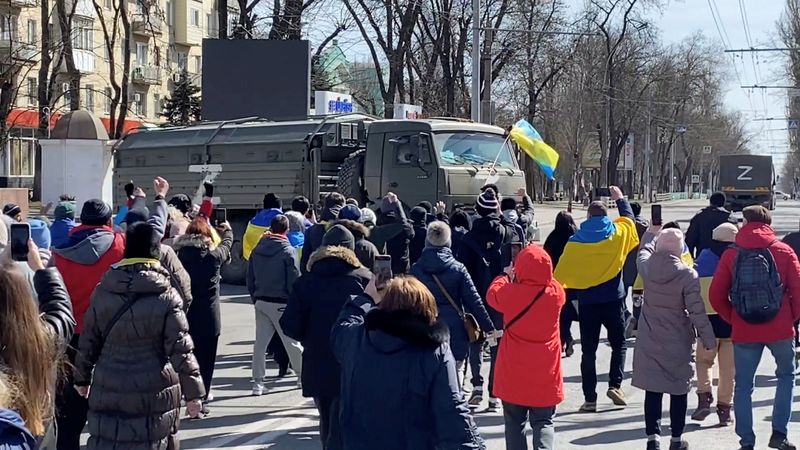 Demonstrators, some displaying Ukrainian flags, chant "go home" while walking towards retreating Russian military vehicles at a pro-Ukraine rally amid Russia's invasion, in Kherson on March 20, 2022.&nbsp; (VIA REUTERS)