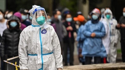A worker wearing protective gear looks on as people wait to be tested for the Covid-19 coronavirus at a residential compound in Shanghai. (AFP)
