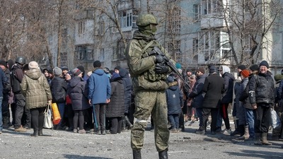 A Russian army soldier stands next to local residents who queue for humanitarian aid delivered during Ukraine-Russia conflict, in the besieged southern port of Mariupol, Ukraine. (REUTERS)