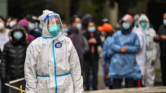 A worker wearing protective gear looks on as people wait to be tested for the Covid-19 coronavirus at a residential compound in Shanghai.(AFP) A worker wearing protective gear looks on as people wait to be tested for the Covid-19 coronavirus at a residential compound in Shanghai.(AFP)