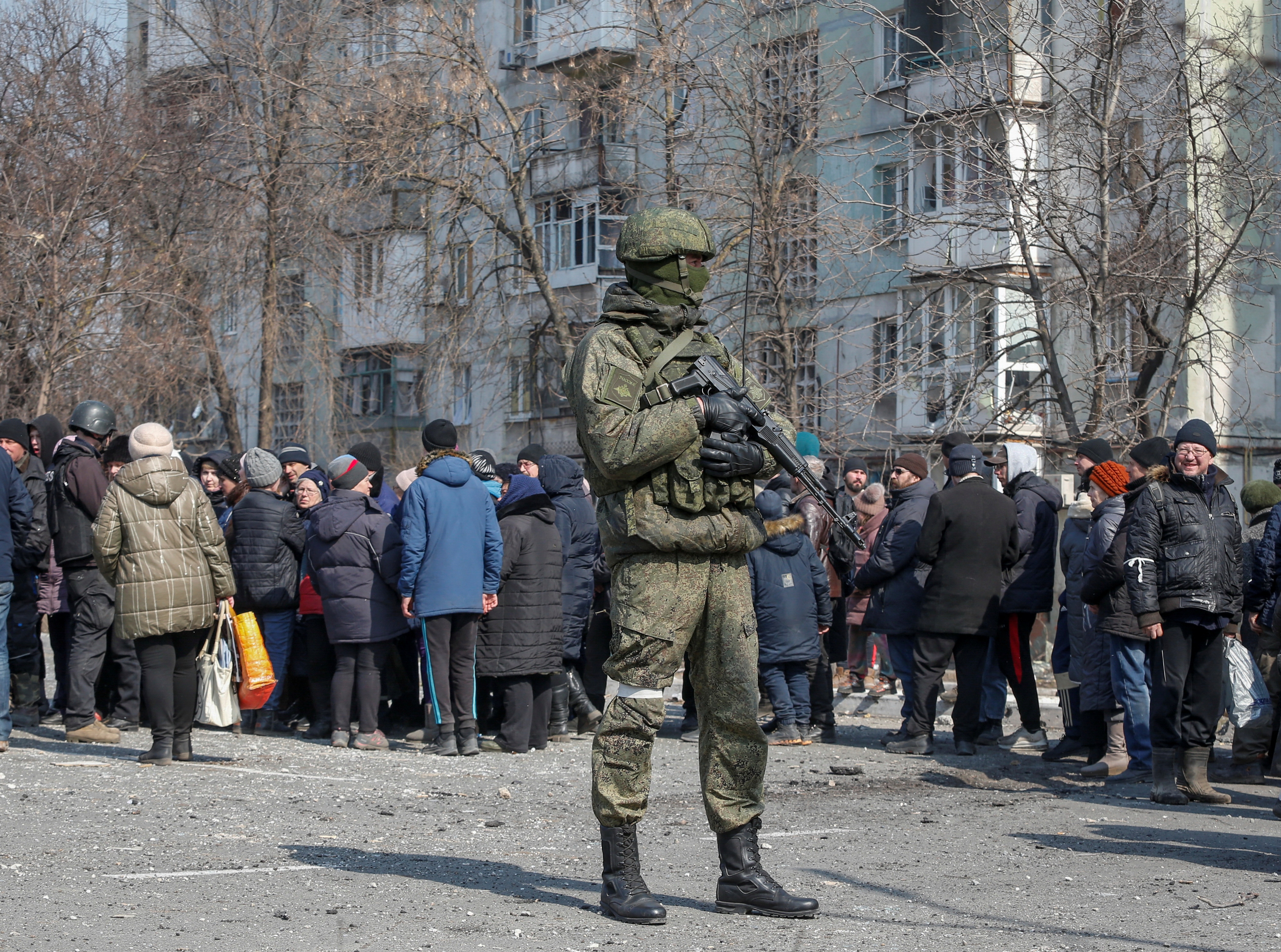 A Russian army soldier stands next to local residents who queue for humanitarian aid delivered during Ukraine-Russia conflict, in the besieged southern port of Mariupol, Ukraine. (Reuters)