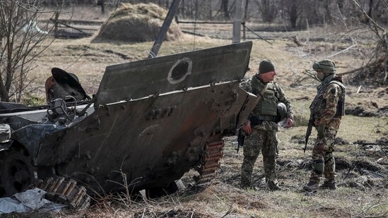 Ukrainian servicemen stand near the wreck of a Russian Armoured Personnel Carriers (APC) on the front line in the Kyiv region, Ukraine March 28, 2022. (REUTERS/Gleb Garanich)