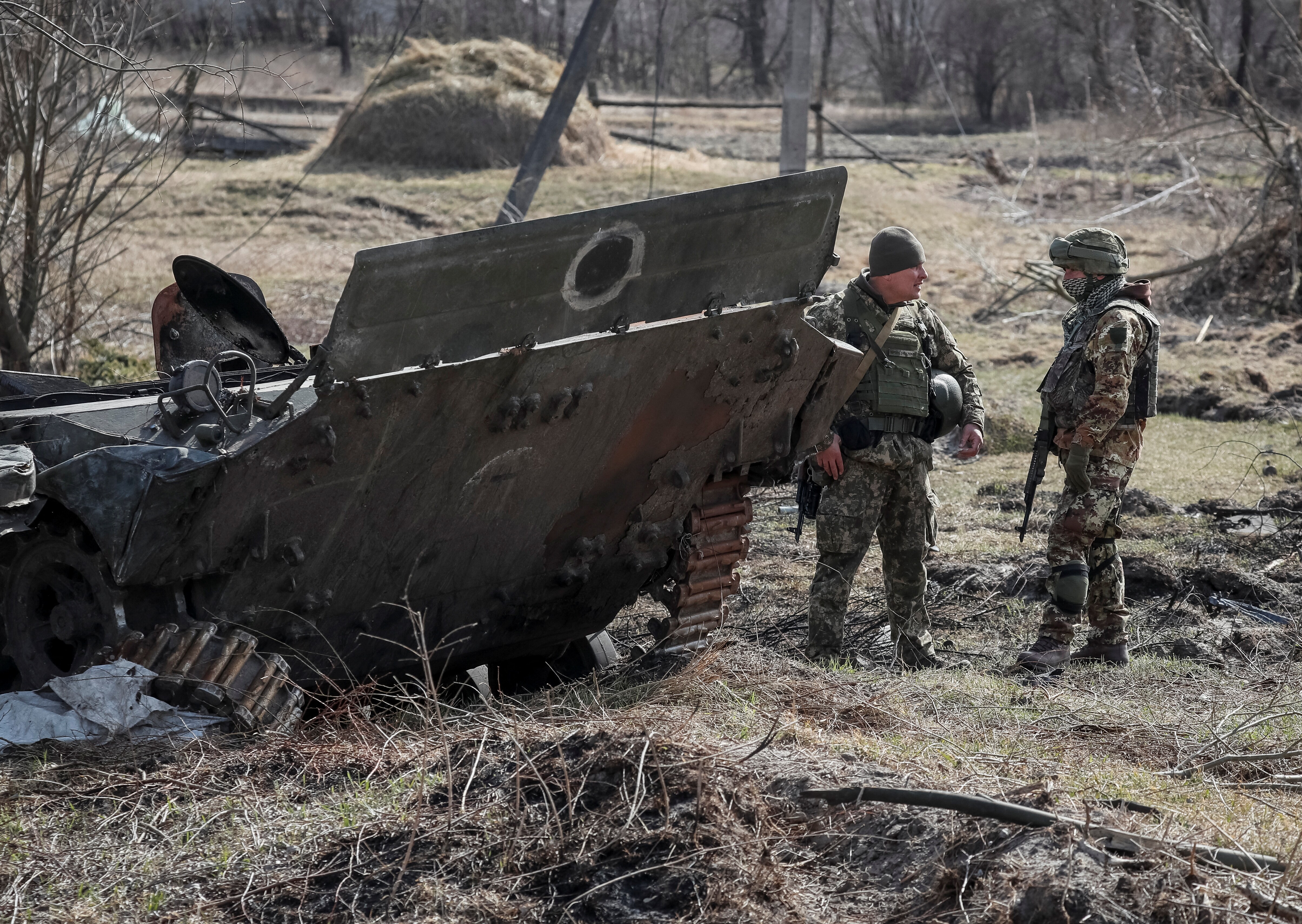 Ukrainian servicemen stand near the wreck of a Russian Armoured Personnel Carriers (APC) on the front line in the Kyiv region, Ukraine March 28, 2022. (REUTERS/Gleb Garanich)
