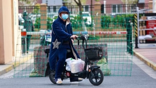 A man rides past a roadblock with his deliveries at a residential community under lockdown in Shanghai, China,(AP)