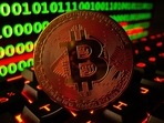 Bitcoin cryptocurrency representation is pictured on a keyboard in front of binary code.