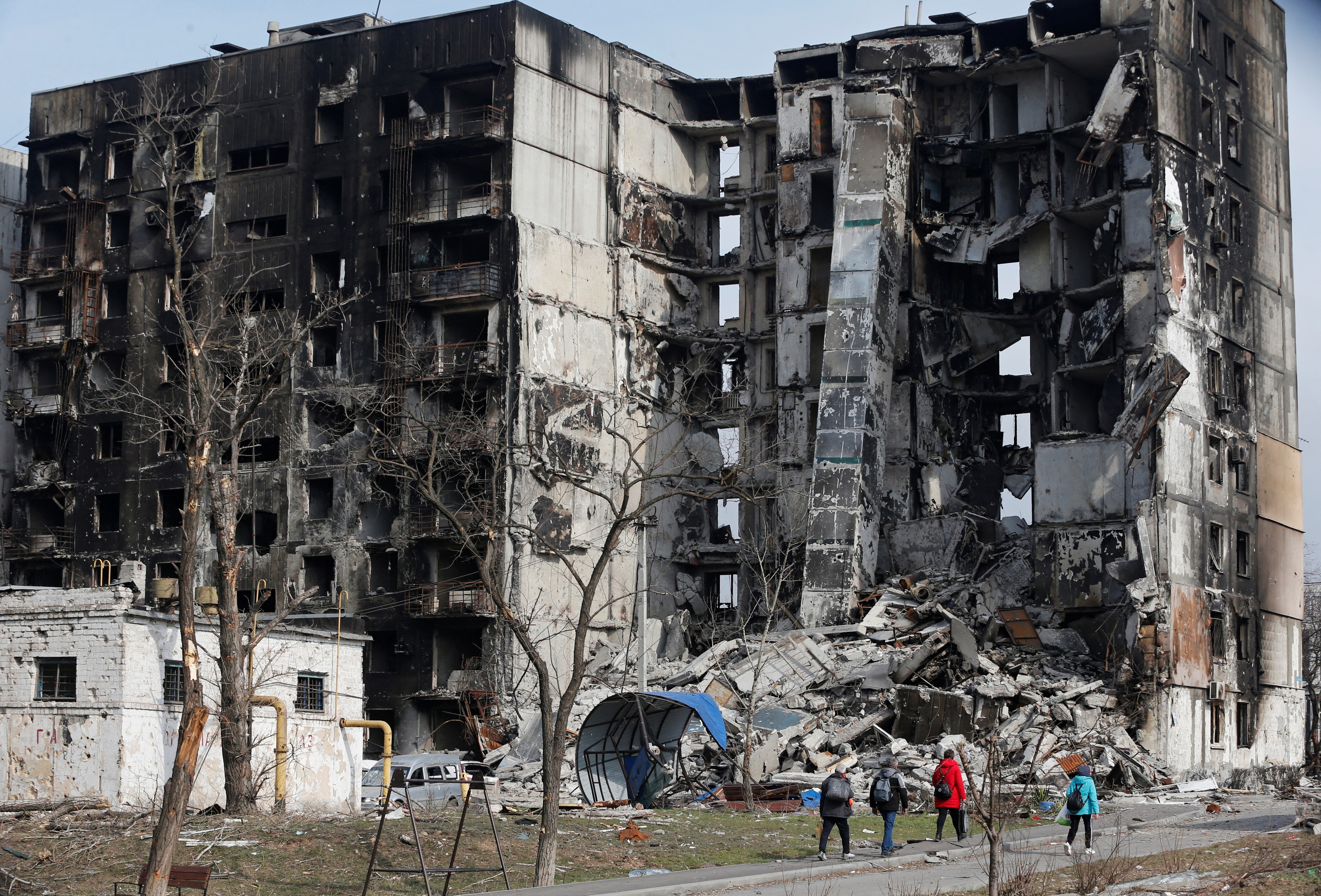 Local residents walk near an apartment building destroyed during Ukraine-Russia conflict in the besieged southern port city of Mariupol on March 30, 2022.&nbsp; (Reuters)