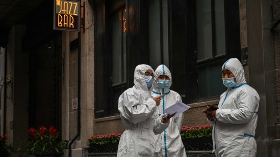 Workers, wearing protective gear, stand next to the access of a hotel on the Bund, in the Puxi area that will be in lockdown from April 1, in Shanghai&nbsp;(Photo by Hector RETAMAL / AFP)